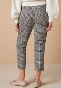 Zwart-witte geruite enkellange broek met een slanke pasvorm, voorzien van zijzakken en een gladde textuur. Draagt met beige ballerina's.