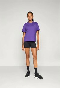 Violet krāsas kokvilnas T-krekls ar īsām piedurknēm, brīvs piegriezums un neliela logo detaļa, kombinēts ar melniem motokrosa šortiem un melnām sporta kurpēm.