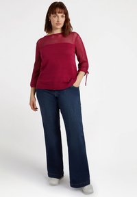 Magenta stickad tröja med ett texturerat mönster, trekvartsärmar och knyt-detajl, i kombination med mörkblå vida jeans och vita sneakers.