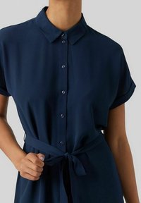 Abito blu navy a maniche corte con colletto, chiusura frontale con bottoni e vita legata. Realizzato in tessuto leggero, presenta una texture liscia.