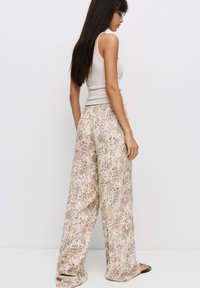 Un débardeur beige associé à un pantalon ample et léger avec un motif léopard marron. Le pantalon a une coupe décontractée et un léger brillant.