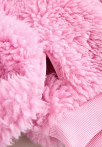 Roze donzige fleecestof met een gestructureerd oppervlak, voorzien van geribbelde manchetten. De levendige kleur benadrukt het pluizige uiterlijk en de zachtheid.
