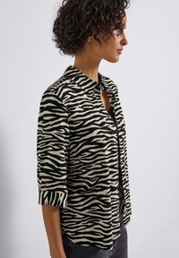 Chemise à imprimé zèbre noir et blanc avec un col, des manches courtes et une coupe légèrement ample, fabriquée à partir d'un tissu doux et léger.