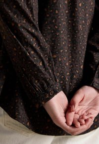 Brown leopard print shirt featuring a relaxed fit, buttoned cuff detail, and gathered sleeve for texture contrast against a light background.