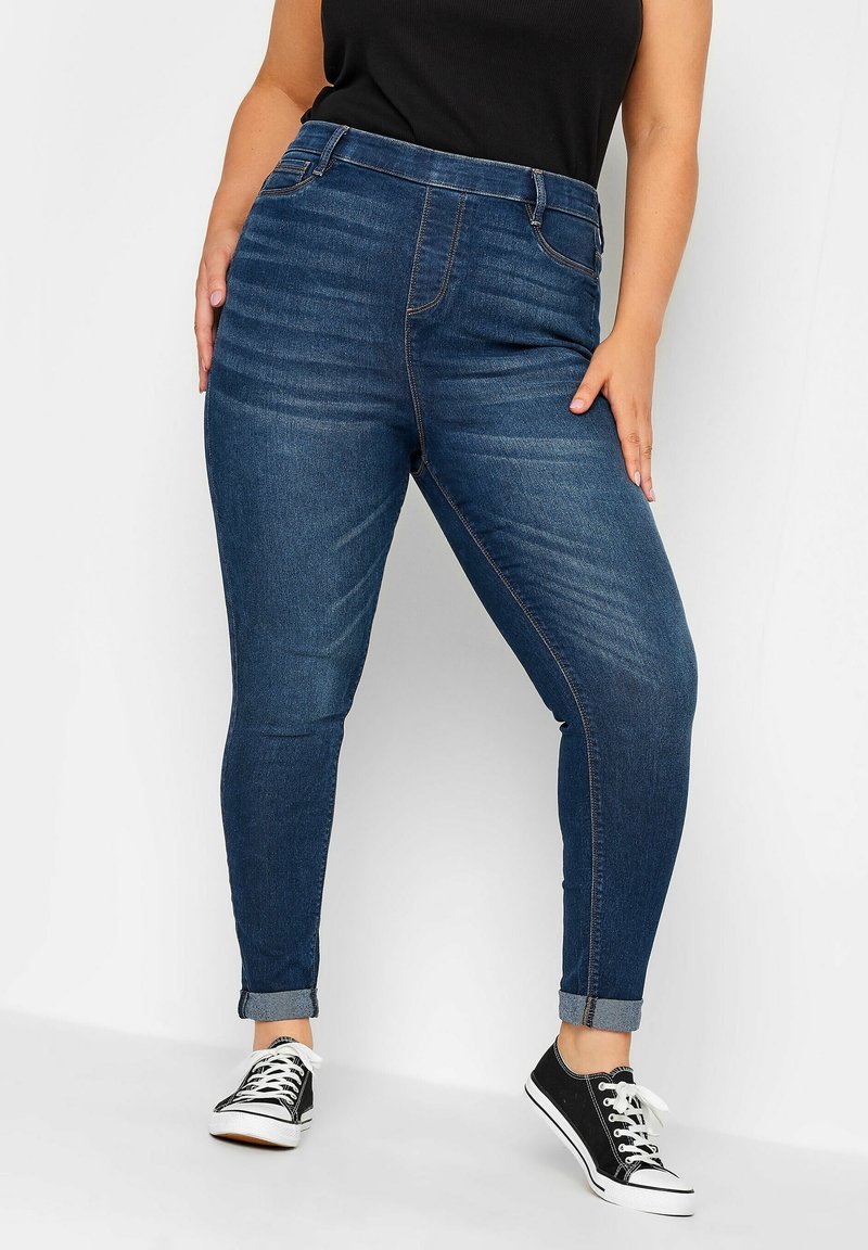 Mörkblå denim skinny jeans med hög midja, fem fickor och uppvikta fållar, kombinerade med svarta canvas sneakers.