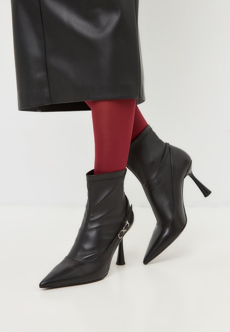 Černé kožené kotníkové boty s špičatou špičkou, stiletto podpatkem a předním řasením, s kovovými detaily v odstínu stříbra na boku.