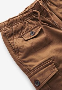 Brune cargo-shorts med elastisk talje, snor, sidelommer og knapdetalje på lommen. Glat stoftekstur.