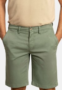 Pantalones cortos de hombre en verde oliva, fabricados en un tejido ligero y suave, con un corte clásico. Presenta bolsillos frontales y un cierre de botón.