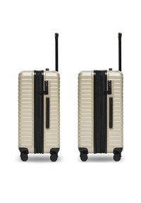 Deux valises rigides beiges avec des poignées noires, des roues, des poignées télescopiques rétractables et des serrures à combinaison intégrées, présentées côte à côte.