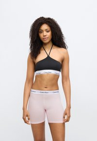 Μαύρο bralette με halter λουρί και λευκή λωρίδα Calvin Klein, συνδυασμένο με ανοιχτό ροζ σορτς μποξέρ με παρόμοια λωρίδα. Λεία υφή, εφαρμοστό σχέδιο.