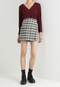 Top a maniche lunghe color bordeaux con scollatura a V; gonna mini in plaid bianco e nero; stivali neri con lacci e suola spessa.