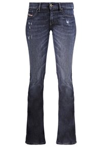 Jean bootcut bleu foncé avec légère usure sur le devant et des zones décolorées sur les cuisses et les genoux, avec poches avant et arrière.