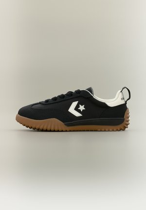 Schwarzer Sneaker mit niedrigem Schaft, weißem Stern-Logo, weißem Fersenlaschen, schwarzen Schnürsenkeln und brauner, profillierter Sohle, auf neutralem Hintergrund abgebildet.