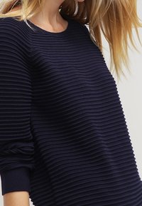 Maglione a coste navy con linee testurizzate orizzontali, scollo rotondo e maniche lunghe. Tessuto morbido e vestibilità rilassata.