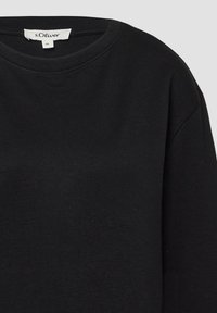 Czarna koszulka z długim rękawem typu crew neck z metką marki s.Oliver oraz etykietą rozmiaru 36 wewnątrz kołnierza.