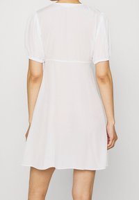 Vestido corto blanco con mangas abullonadas, confeccionado en una tela ligera y texturada, con escote redondo y una silueta acampanada que termina por encima de la rodilla.