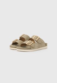 Olive green suede sandals with two buckled straps, a textured footbed, and a light brown sole featuring a zigzag tread pattern.