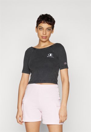 Top corto nero a coste con maniche corte e logo Champion sul petto, abbinato a pantaloni shorts con vita elastica di un rosa chiaro, dotati di tasche.