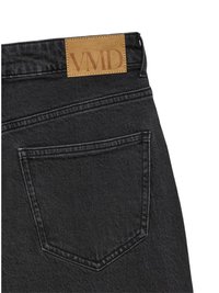 Fekete farmernadrág barna bőr címkével, amin a "VMD" felirat olvasható. Egyetlen hátsó zsebében finom varrási részletek láthatók.