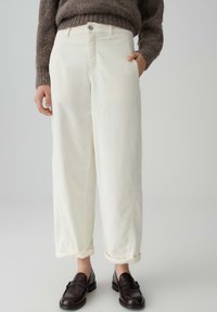 Pantaloni in denim bianco con una vestibilità rilassata, orli arrotolati e tasche laterali. Abbinati a mocassini marrone scuro e un maglione marrone a trama.