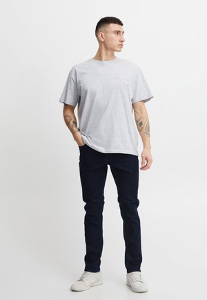 Graues Baumwoll-T-Shirt mit kurzen Ärmeln, rundem Ausschnitt, lockerer Passform und dezentem roten Text. Kombiniert mit dunkelblauen Slim-Fit-Jeans und weißen Turnschuhen.