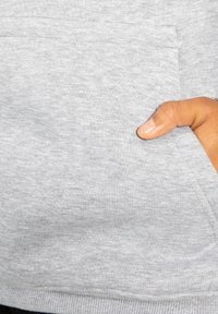 Sweat-shirt gris clair avec une texture douce, doté d'une poche avant et d'une main visible reposant sur le bord de la poche.