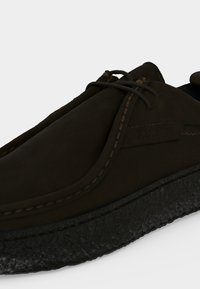 Gros plan d'une chaussure décontractée en daim brun foncé avec des détails cousus et une semelle noire épaisse et texturée.