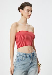 Cropped top senza spalline a righe rosse e bianche, con texture a coste e design leggermente aderente. Indossato con jeans in denim azzurro a vita alta.