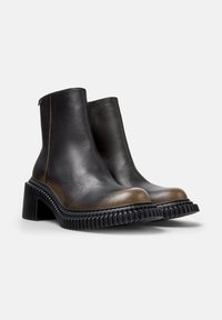 Botas de cuero negras hasta el tobillo con punta redondeada y una puntera marrón de contraste. Suela de goma negra gruesa con textura acanalada, detalle de costura mínimo.