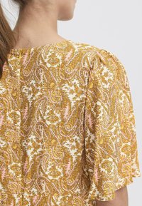 Rochie cu mânecă scurtă, având un model paisley în nuanțe de galben și roz, din material moale, cu decolteu rotund și un fermoar discret la spate.