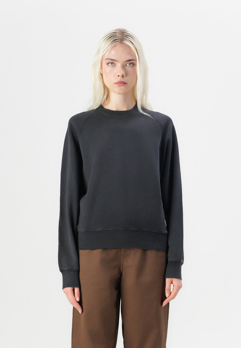 Sweatshirt negru din bumbac cu mâneci raglan, cu mansete și tiv din material ribat. Stilizat cu pantaloni largi maro. Textură netedă, design minimalist.