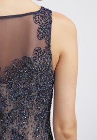 Black tulle dress featuring intricate, beaded floral embroidery with shimmering accents along the neckline and upper back.