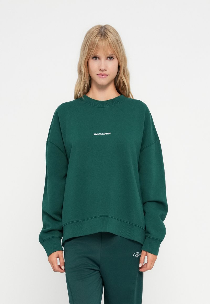 Felpa verde con scollatura rotonda e spalle cadenti. Presenta un logo bianco "PEGADOR" sul petto. Tessuto morbido e vestibilità comoda.