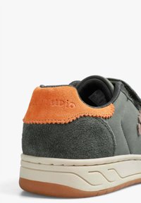 Zapatilla de ante gris con un acento trasero naranja, con un talón texturizado y una suela blanca con un patrón de diseño sutil.