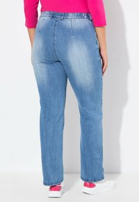 Jeans de mezclilla azul claro con cintura elástica, diseño de pierna recta y un ligero desgaste. Combinados con zapatillas blancas con detalles en rosa.