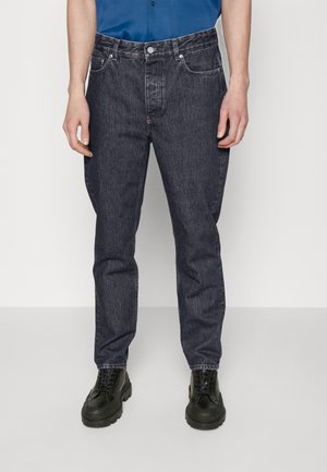 Jeans de mezclilla azul oscuro con corte recto, diseño de cinco bolsillos y detalles de costura. Combinados con botas negras de cordones.