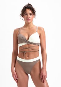 Bikini a due pezzi con un top avvolgente in marrone e crema, dotato di spalline regolabili e una finitura testurizzata. La parte inferiore è coordinata ed è alta in vita.