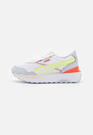 Weißer Puma-Sneaker mit hellgrauen Akzenten, neongelben Streifen, orangen Details und dicker weißer Sohle, seitlich gezeigt.