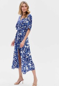 Niebieska i biała sukienka w kwiatowy wzór z krótkimi rękawami, zapinana na krzyż, z paskiem w talii i rozcięciem do uda. Gładka tekstura.