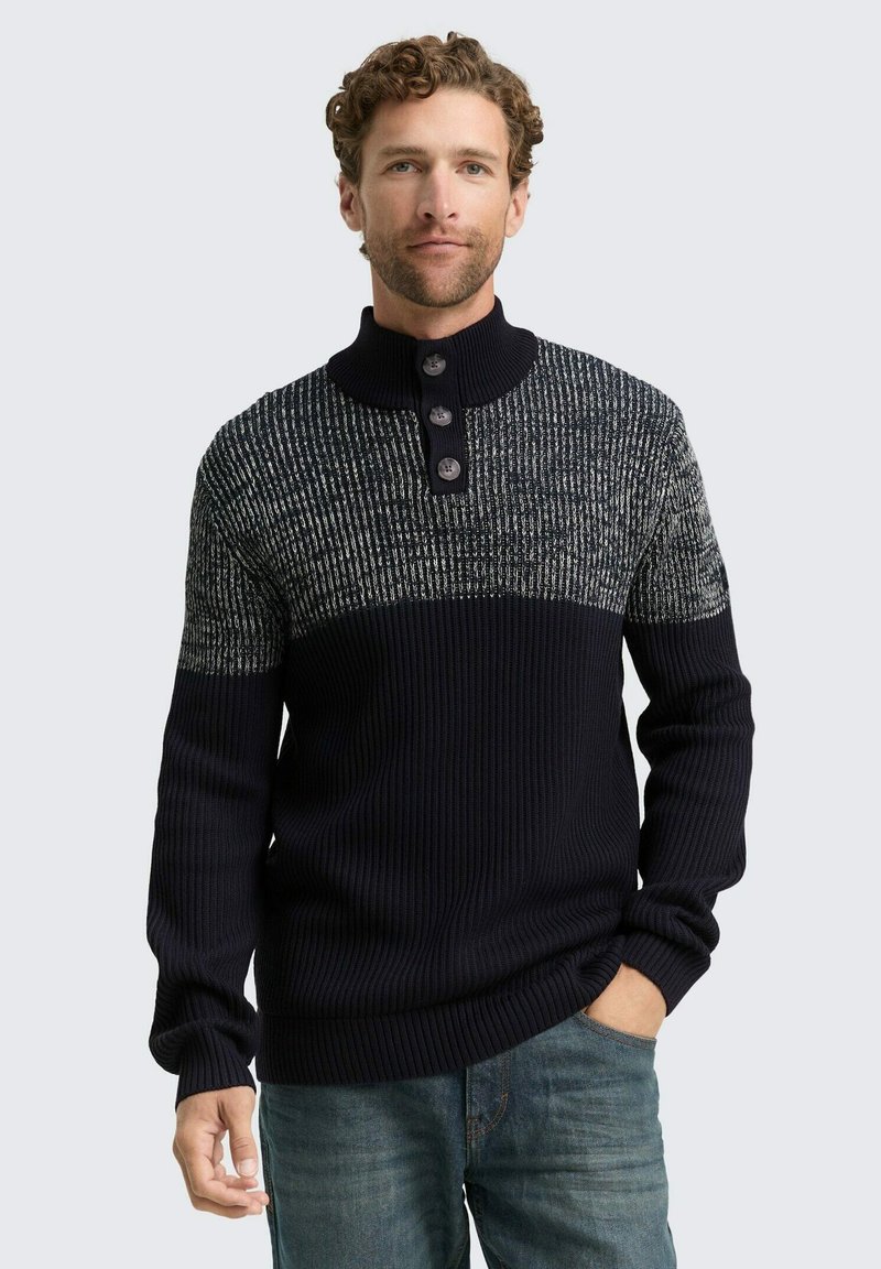 Navyblauer Strickpullover mit einer strukturierten grauen Oberseite, ausgestattet mit einem Stehkragen und einem Drei-Knopf-Verschluss. Gerippte Bündchen und Saum.
