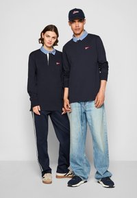 Navy long-sleeve polo with blue chambray collar; red logo detail. Pair with navy track pants and faded blue jeans, sporty sneakers.