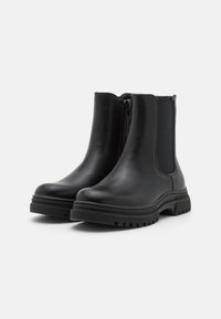 Bottines en cuir noir avec une finition lisse, panneaux élastiques sur les côtés et une semelle en caoutchouc robuste. Équipées d'une fermeture éclair pour un enfilage facile.