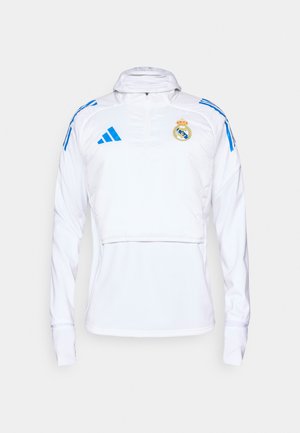 Sudadera atlética blanca con mangas largas, cuello con media cremallera y acentos en azul. Presenta el escudo del Real Madrid y los logotipos de Adidas. Textura suave.
