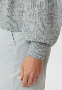 Jasnoszary sweter z dzianiny o fakturowanych, puszystych rękawach i ściągaczach, zestawiony z jasnoszarymi spodniami materiałowymi z boczną kieszenią.