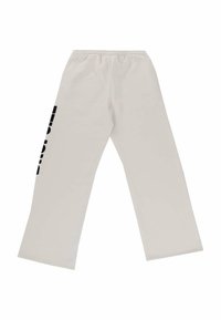 Gai bēša krāsa sporta bikses, izgatavotas no mīksta auduma, ar melnu grafisku apdruku uz kreisās kājas un elastīgu vidukļa joslu. Ar platām kājām.