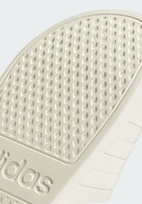 White rubber sneaker sole with a textured, dimpled pattern, featuring a raised brand logo and horizontal stripes for traction.