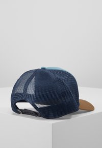 Jūras spēku tīkla beisbola cepure ar gaiši zilu priekšējo paneli un brūnu vizieri. Aprīkota ar regulējamu snapback aizdari.