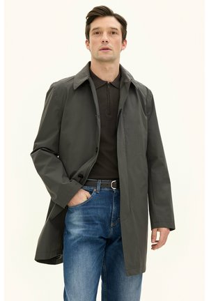 Cappotto leggero grigio scuro con colletto, chiusura a bottoni e tasche laterali, indossato sopra una maglietta polo marrone e jeans di denim blu.