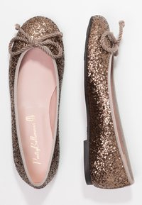 Bailarinas de bronce con brillo, puntera redondeada, ribete elástico y un lazo decorativo hecho de cuerda trenzada. Plantilla interior rosa visible.