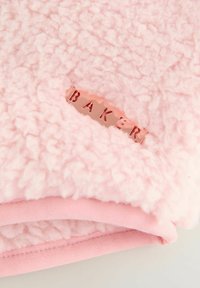 Couverture rose et moelleuse avec une surface texturée et shaggy. Présente une doublure lisse et une étiquette métallisée couleur or rose portant l'inscription "BAKERI."